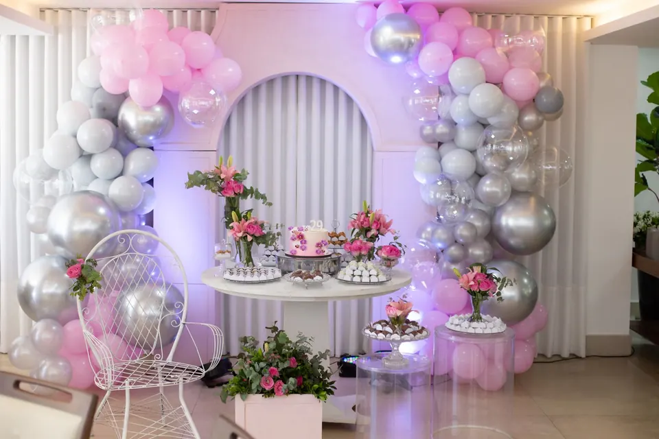 Arco de globos plateados y rosas con una mesa de fiesta